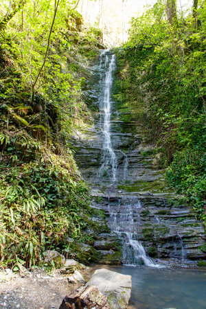 A waterfall is flowing down a rocky cliff. The water is clear and the rocks are brown. The scene is peaceful and sereneの写真素材