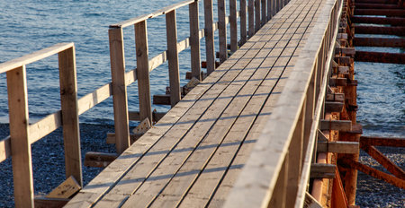 A wooden pier with a wooden walkway leading to the water. The pier is empty and the water is calmの写真素材