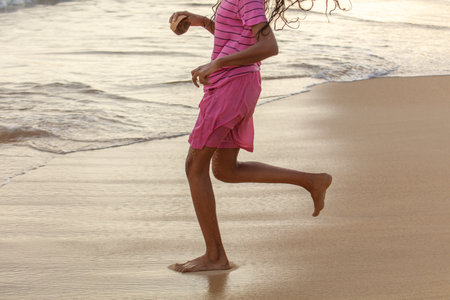 A girl is running on the beach in a pink dress. She is holding a coconut in her handの写真素材