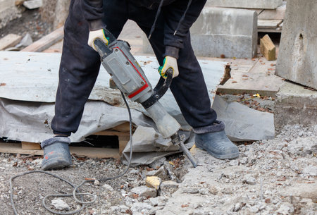 A man is using a jackhammer to break up concrete. Concept of hard work and determination, as the man is focused on his task despite the challenging conditionsの写真素材