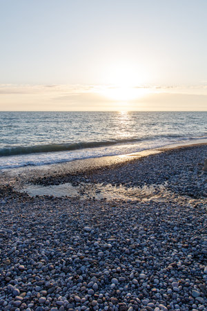 A beach with a large body of water and a large rock field. The sun is setting and the sky is a beautiful blue colorの写真素材