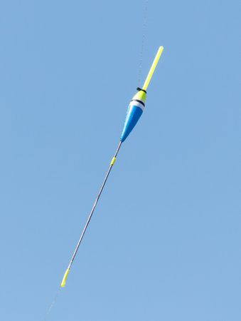 A blue and yellow buoy is floating in the air. The buoy is attached to a string and is being flown by a person. The sky is clear and blue, and the buoy is the only object in the sceneの写真素材