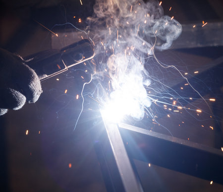 A person is welding a piece of metal, and the sparks are flying. Concept of danger and excitement, as the welder is working with intense heat and bright light. The sparks and smoke create a dramaticの写真素材