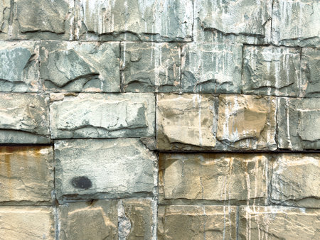 A wall made of stone with a few cracks and some water stains. The wall is gray and has a rough textureの写真素材