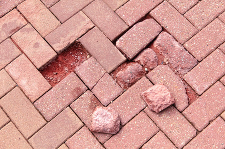 A brick sidewalk with a large hole in it. The bricks are scattered around the hole. The hole is large enough to fit a personの写真素材