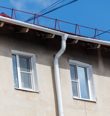 A white house with a red roof and a white pipe coming out of the roof. The pipe is attached to the side of the houseの写真素材