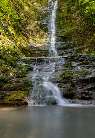 A waterfall is flowing down a rocky cliff. The water is clear and calm. The scene is peaceful and sereneの写真素材
