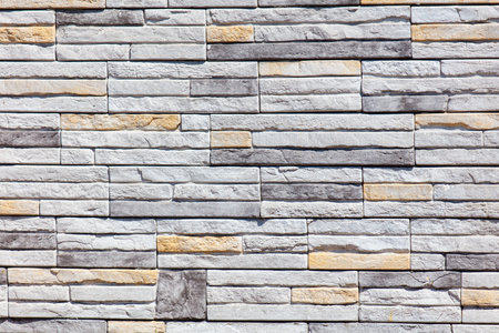A wall made of gray and white bricks. The wall is made of many different sized bricks. The wall is very plain and has no decorationの写真素材