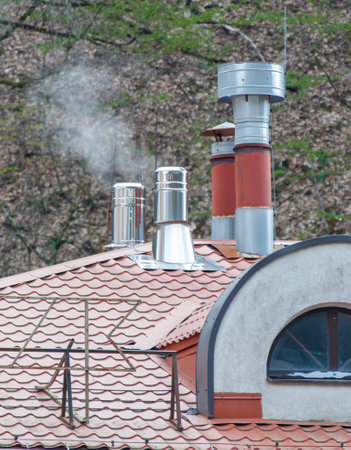 A house with a red roof and a chimney. The chimney is smoking and the roof is covered in leavesの写真素材