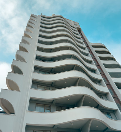 A tall building with a white facade and a blue sky in the background. The building has a unique design with a wave-like shapeの写真素材