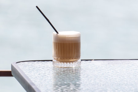 A glass of liquid with a straw in it sits on a table. The glass is half full and the straw is...