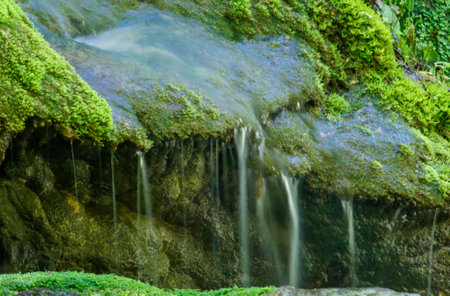 A rock covered in moss and water dripping from it. The water is clear and the moss is greenの写真素材