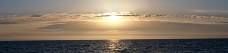 The sun is setting over the ocean, casting a warm glow on the water. The sky is a mix of blue and orange, creating a serene and peaceful atmosphereの写真素材