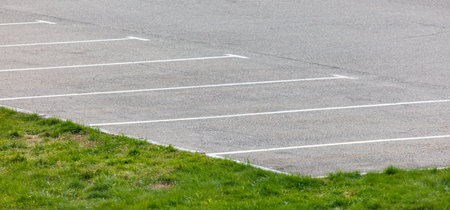 A parking lot with white lines and grass. The parking lot is empty and the grass is greenの写真素材
