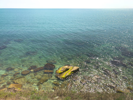A rocky shoreline with a large rock in the water. The water is clear and calm. The rock is partially submerged in the waterの写真素材