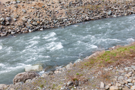 A river with a rocky bank and a lot of water. The water is moving fast and the rocks are scattered around the riverの写真素材