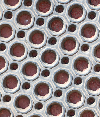 A close up of a patterned surface with many small holes. The holes are red and the surface is grayの写真素材