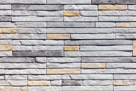 A wall made of white and brown bricks. The wall is made of many different sized bricks. The wall is very textured and has a lot of detailの写真素材