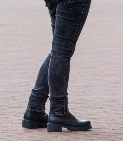 A person wearing black jeans and black boots. The person is standing on a brick surfaceの写真素材
