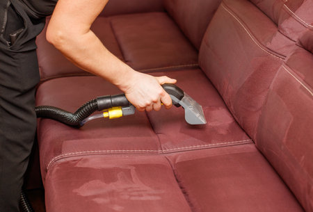 A person is cleaning a couch with a vacuum. The couch is red and has a lot of water on itの写真素材