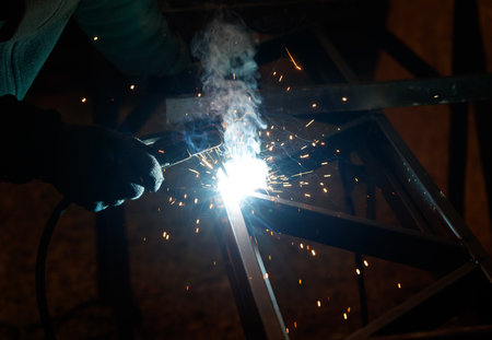 A man is welding metal with a bright light shining on it. Concept of hard work and dedication, as the man is focused on his task. The bright light highlights the sparksの写真素材