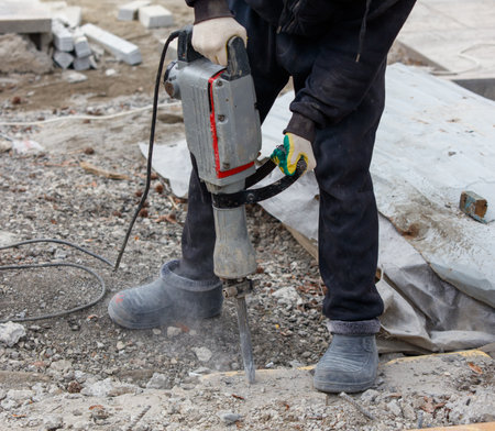 A man is using a jackhammer to break up concrete. Concept of hard work and determination, as the man is focused on his task despite the challenging conditionsの写真素材
