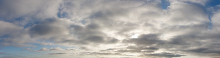 The sky is cloudy and the sun is shining through the clouds. The clouds are white and fluffy, and the sky is blueの写真素材