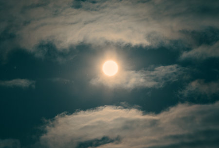The sky is cloudy, and the moon is shining brightly. The clouds are white, and the moon is yellow.の写真素材