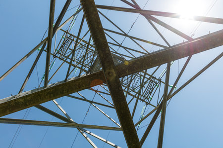A tall metal structure with a blue sky in the background. The structure is a power tower. The sky is clear and bright, and the sun is shining on the towerの写真素材