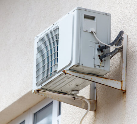 A white air conditioner unit is mounted on a wall. The unit is old and rustyの写真素材