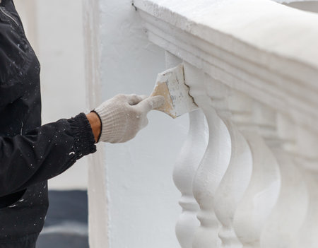 A person is painting a white railing. The railing is made of stone and has a lot of detail. The person is wearing gloves and a black jacketの写真素材