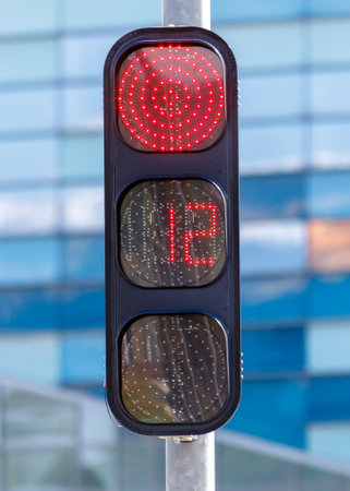 A traffic light with a red circle and the number 12 on it. The traffic light is on a pole next to a buildingの写真素材