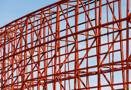 A red structure with many metal beams and a blue sky in the background. The structure is unfinished and is a roller coaster.の写真素材