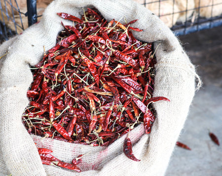 A bag of red peppers is sitting on a table. The peppers are in various sizes and are scattered throughout the bag. The bag is made of burlap and is tied closed. The scene gives off a rusticの写真素材