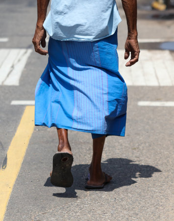 A man wearing a blue skirt walks across a street. Concept of cultural diversity and acceptance, as the man is dressed in traditional clothing while walking on a modern streetの写真素材