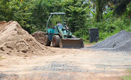A green tractor is in a field of dirt and rocks. The tractor is being used to move the rocks and dirtの写真素材
