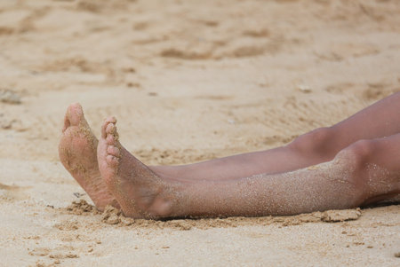 A person's feet are laying in the sand on a beach. The sand is dry and the person is relaxedの写真素材