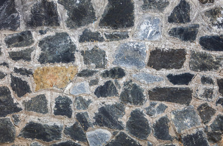 A wall made of stone and gray rocks. The wall is made of many different sized rocks. The wall is very rough and has a lot of textureの写真素材