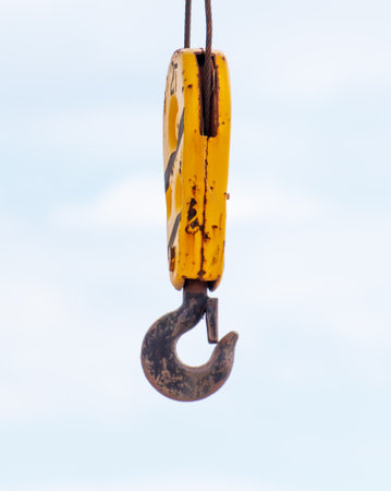 A rusty yellow hook is hanging from a rope. The hook is old and worn, and it is hanging from the ropeの写真素材