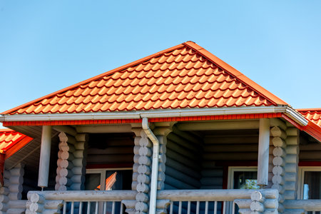 A house with a red roof and a white gutter. The roof is slanted and the house is made of woodの写真素材