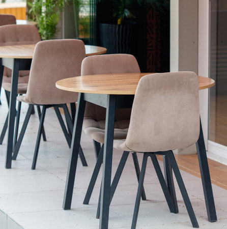 Three chairs are arranged around a round table in a restaurant. The chairs are made of wood and have a tan color. The table is also made of wood and has a brown colorの写真素材