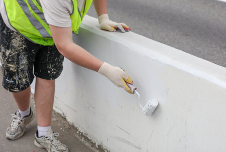 A man in a yellow vest is painting a wall. He is wearing gloves and a safety vestの写真素材