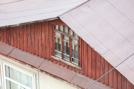 A red house with a window on the roof. The window is open and the roof is covered in snowの写真素材