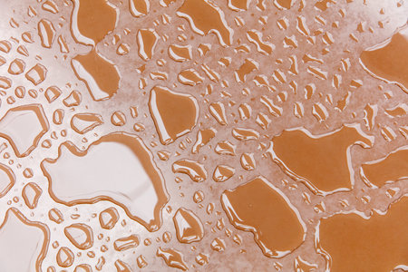 A brown surface with water droplets scattered all over it. The droplets are of various sizes and are spread out in different directionsの写真素材