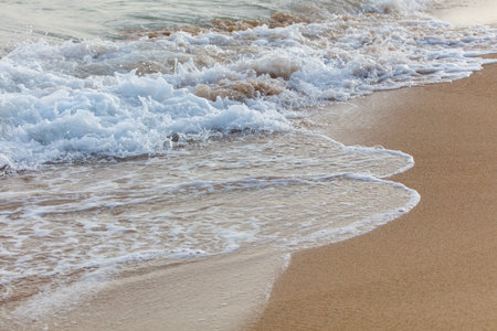 The ocean waves are crashing onto the shore, creating a beautiful and calming scene. The water is a mix of white and brown, giving it a unique and interesting appearance. The beach is emptyの写真素材