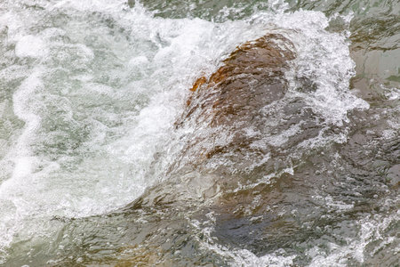 The water is rough and choppy, with a large rock in the middle. The rock is partially submerged in the water, and the waves are crashing against it. The scene is dynamic and powerful, with the waterの写真素材