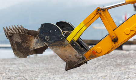A yellow and black construction machine with a yellow handle. The machine is on a rocky beach. The machine is used for digging and moving dirtの写真素材