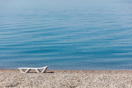 A white beach chair is laying on the sand next to the ocean. The chair is empty and the ocean is calmの写真素材