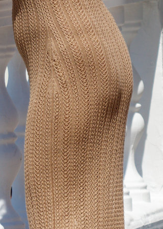 A woman is wearing a tan dress with a white railing in the background. The dress is made of a fuzzy material and has a striped patternの写真素材