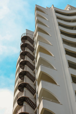 A tall building with a spiral staircase on the side. The building is white and has a blue sky in the backgroundの写真素材